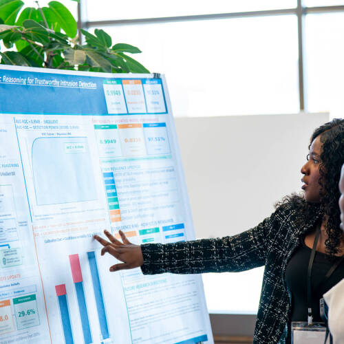 Two computing students view and discuss a research poster at Innovation Day